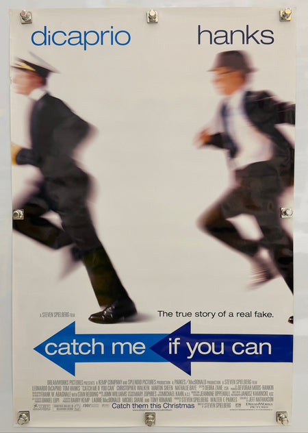 A vintage movie poster for 'Catch Me If You Can' featuring blurred figures of two men in suits, with blue title text and the names 'hanks' and 'dicaprio' printed on a light background.