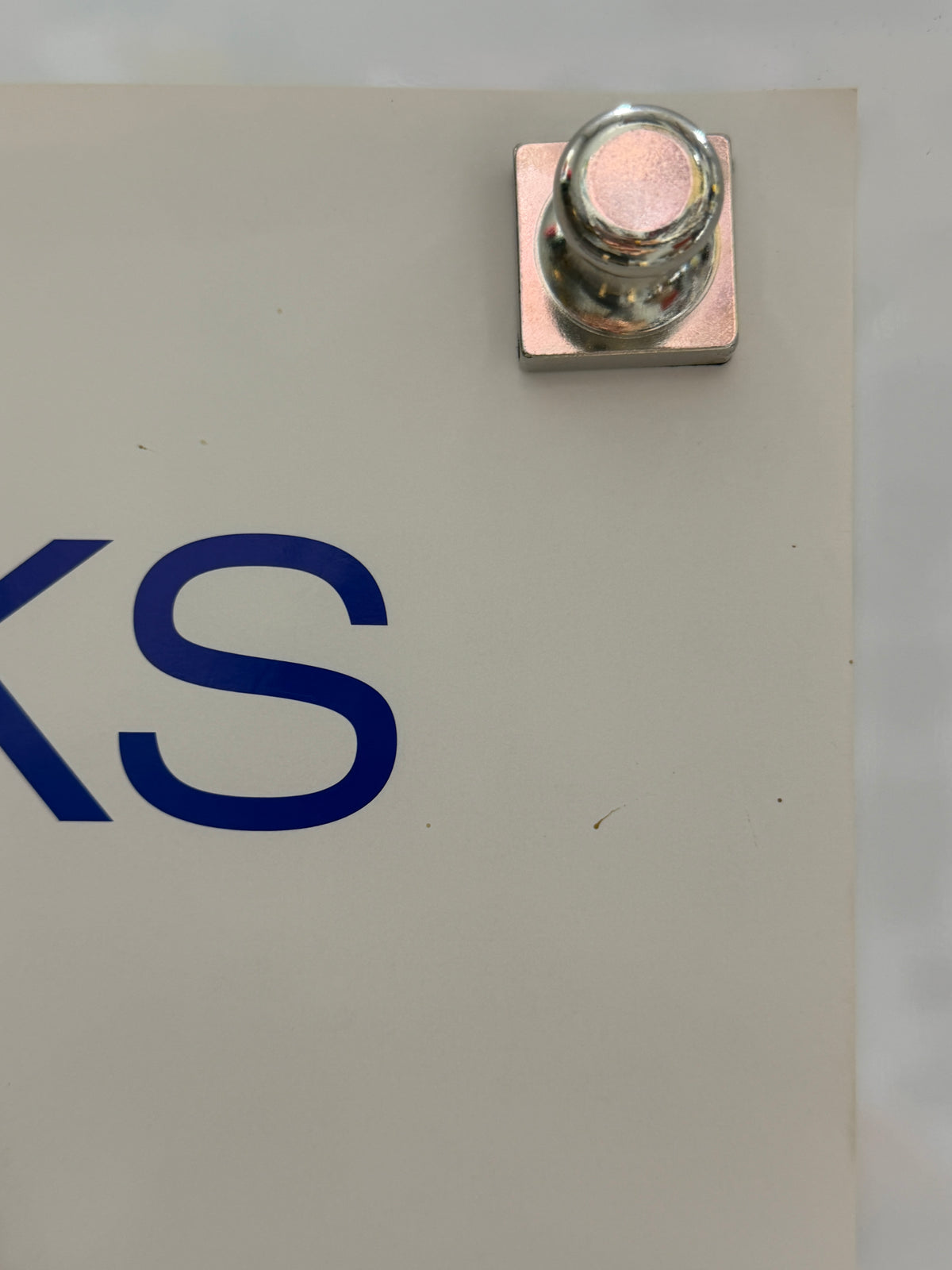 Close-up of a metallic terminal or connector attached to a beige panel with blue printed lettering partially visible.