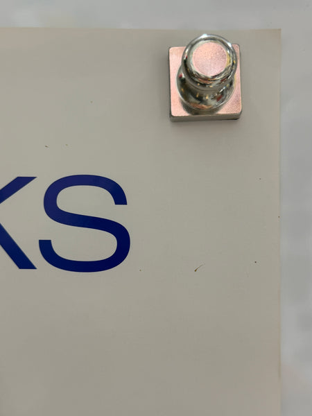 Close-up of a metallic terminal or connector attached to a beige panel with blue printed lettering partially visible.