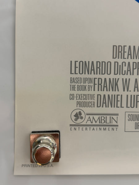 A close-up of a white printed card or booklet with black text including 'Dreamcatcher', 'Leonardo DiCaprio', and 'Amblin Entertainment', plus a small metallic circular object attached near the lower right.
